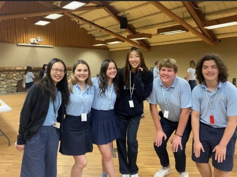 Yi-Hui Chen smiling with a group of Interlochen students in a wood-beamed hall