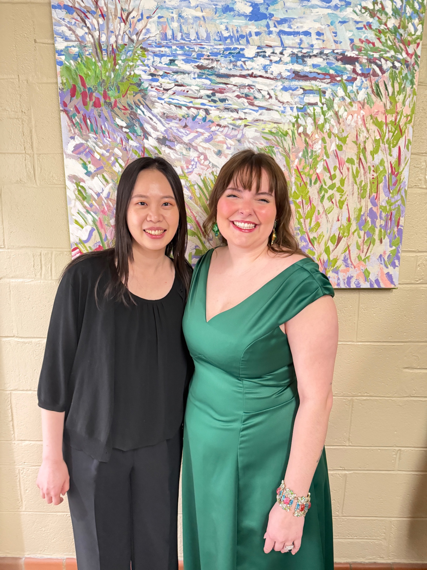 Yi-Hui Chen smiling beside a soprano in a green gown in front of a painting