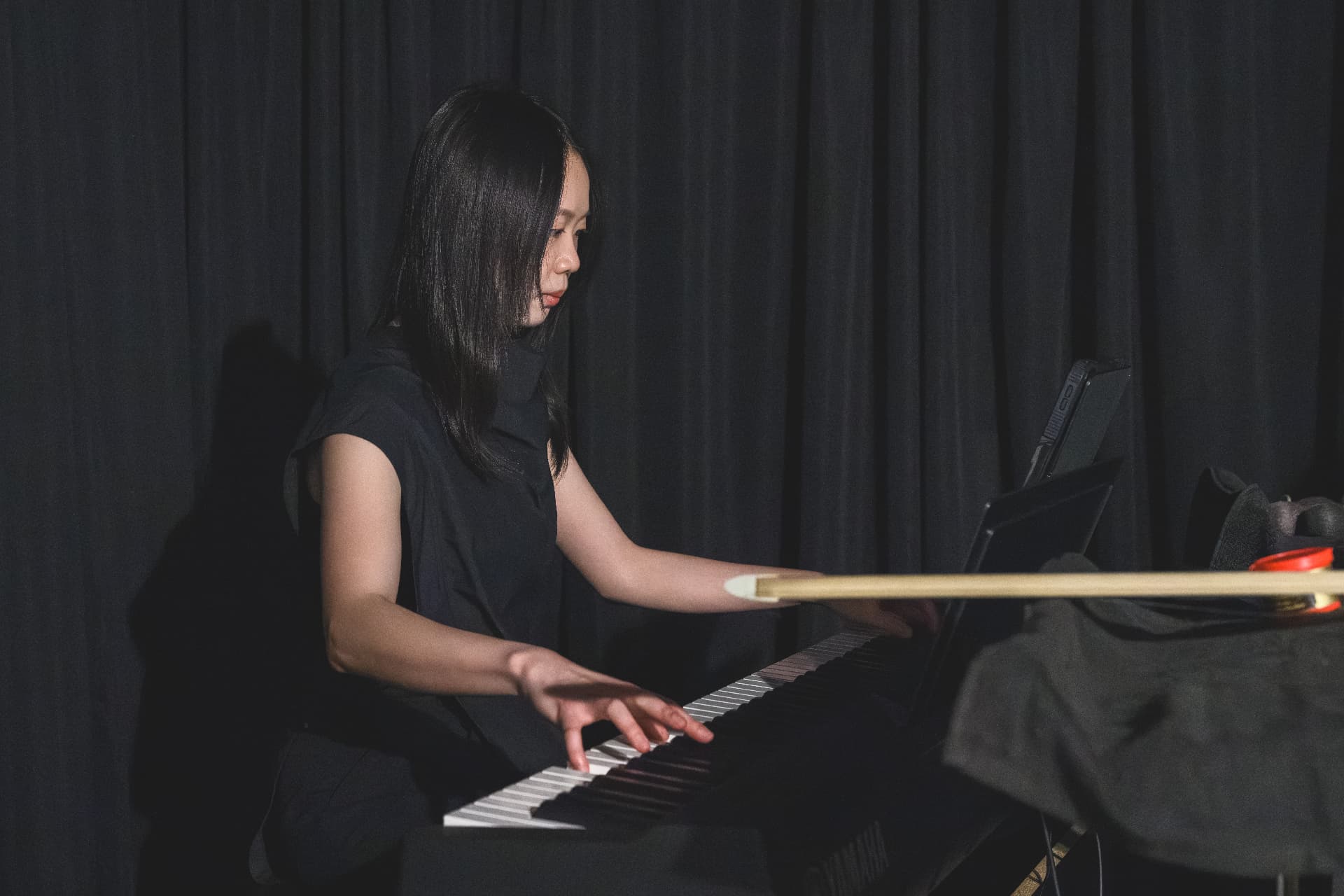 Yi-Hui Chen playing a keyboard against a dark curtain backdrop