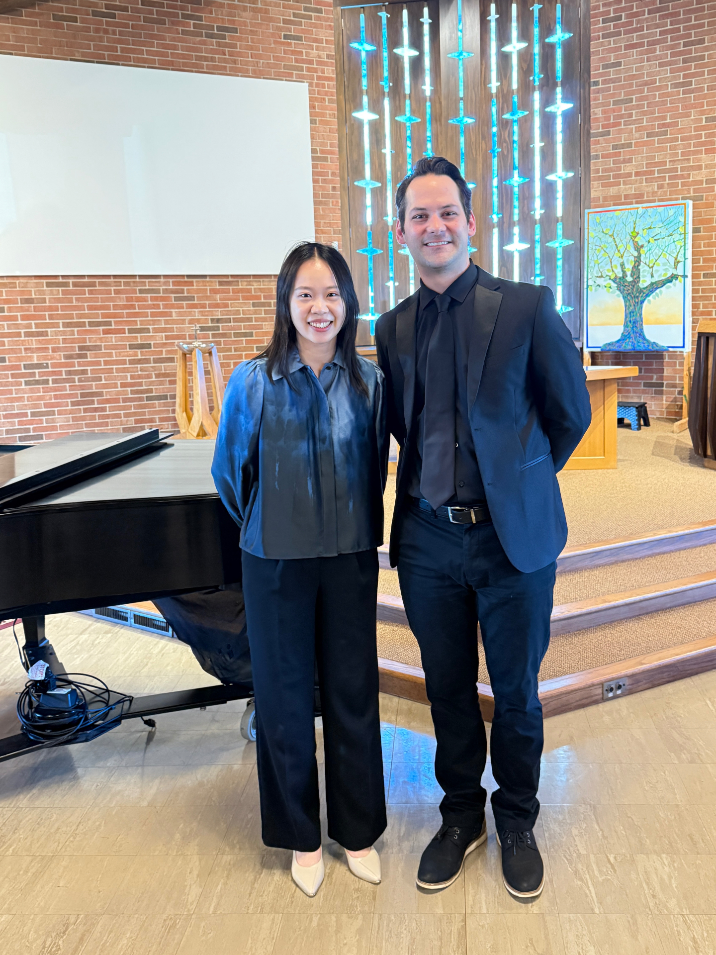 Yi-Hui Chen standing beside a colleague in concert dress beside a grand piano in a church