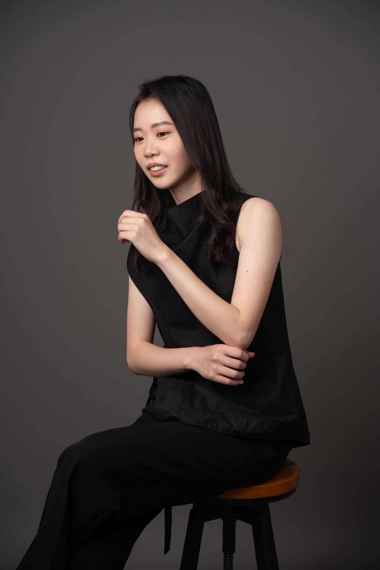 Yi-Hui Chen seated on a stool in black concert attire against a grey backdrop