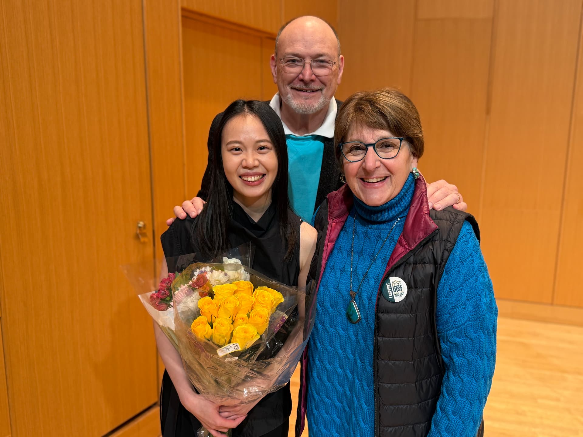 Yi-Hui Chen holding a bouquet of yellow roses with two smiling supporters after a recital