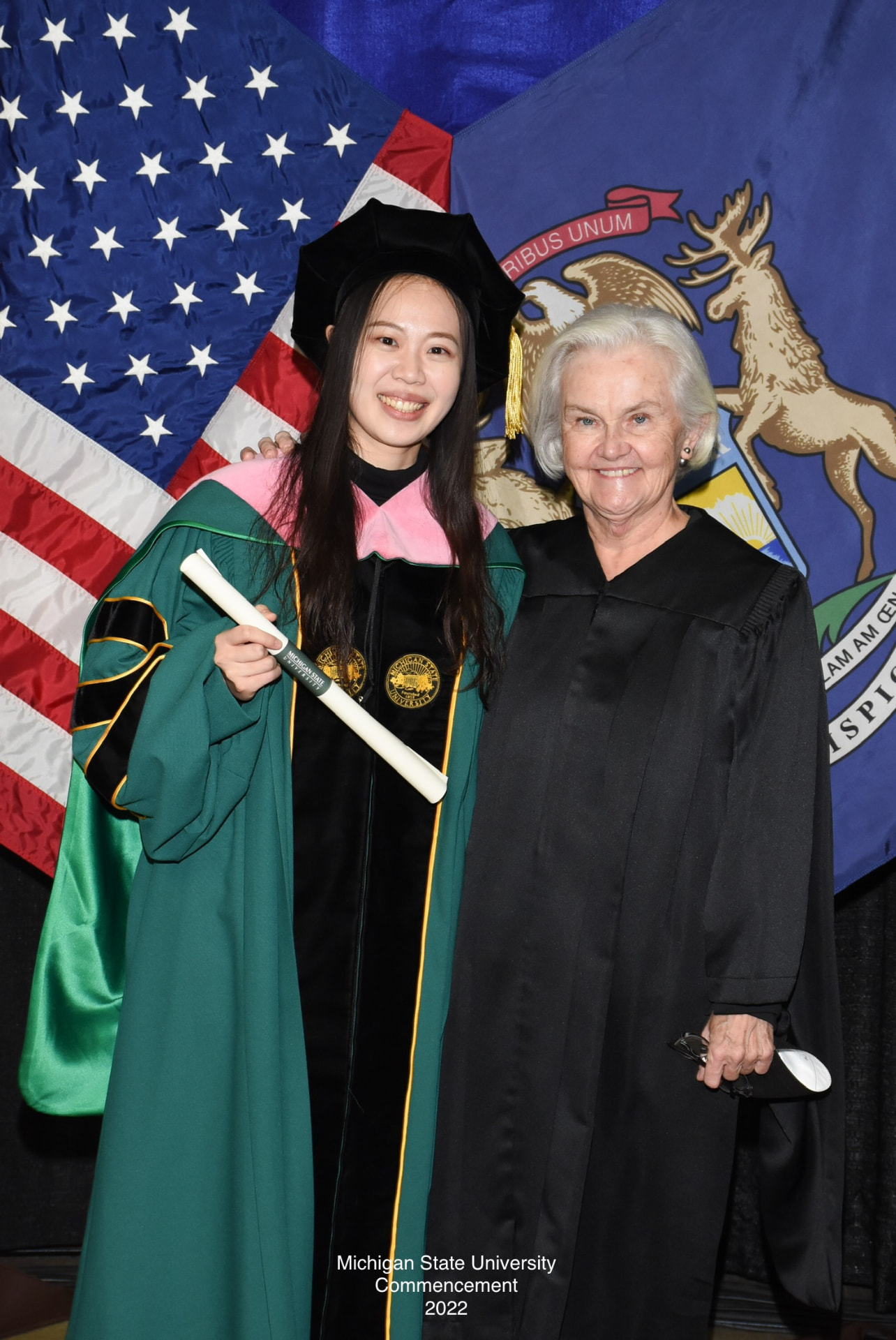 Yi-Hui Chen in doctoral regalia with a diploma beside a faculty member at Michigan State University commencement