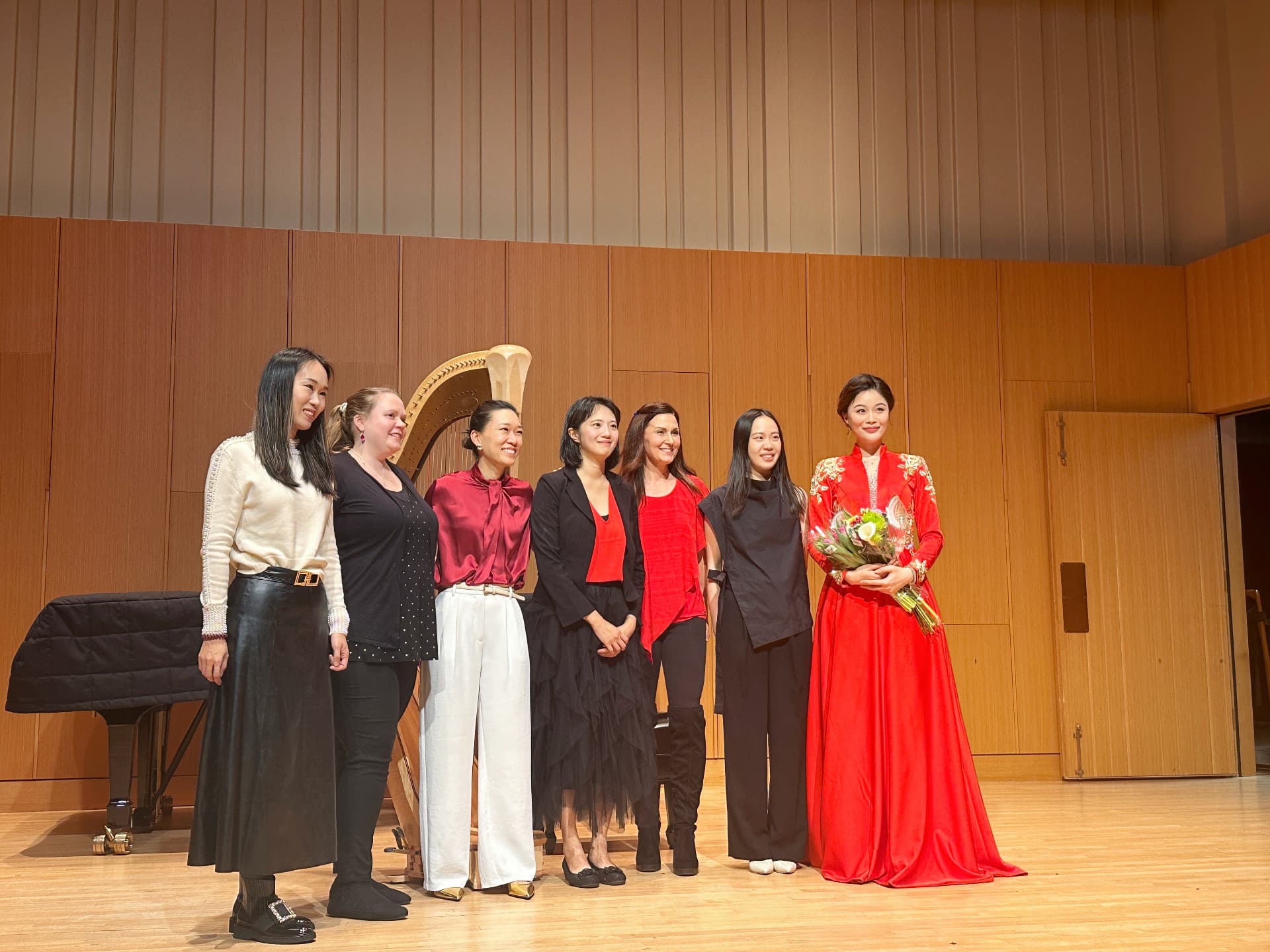Yi-Hui Chen standing on stage with fellow performers, one holding a bouquet in a red gown
