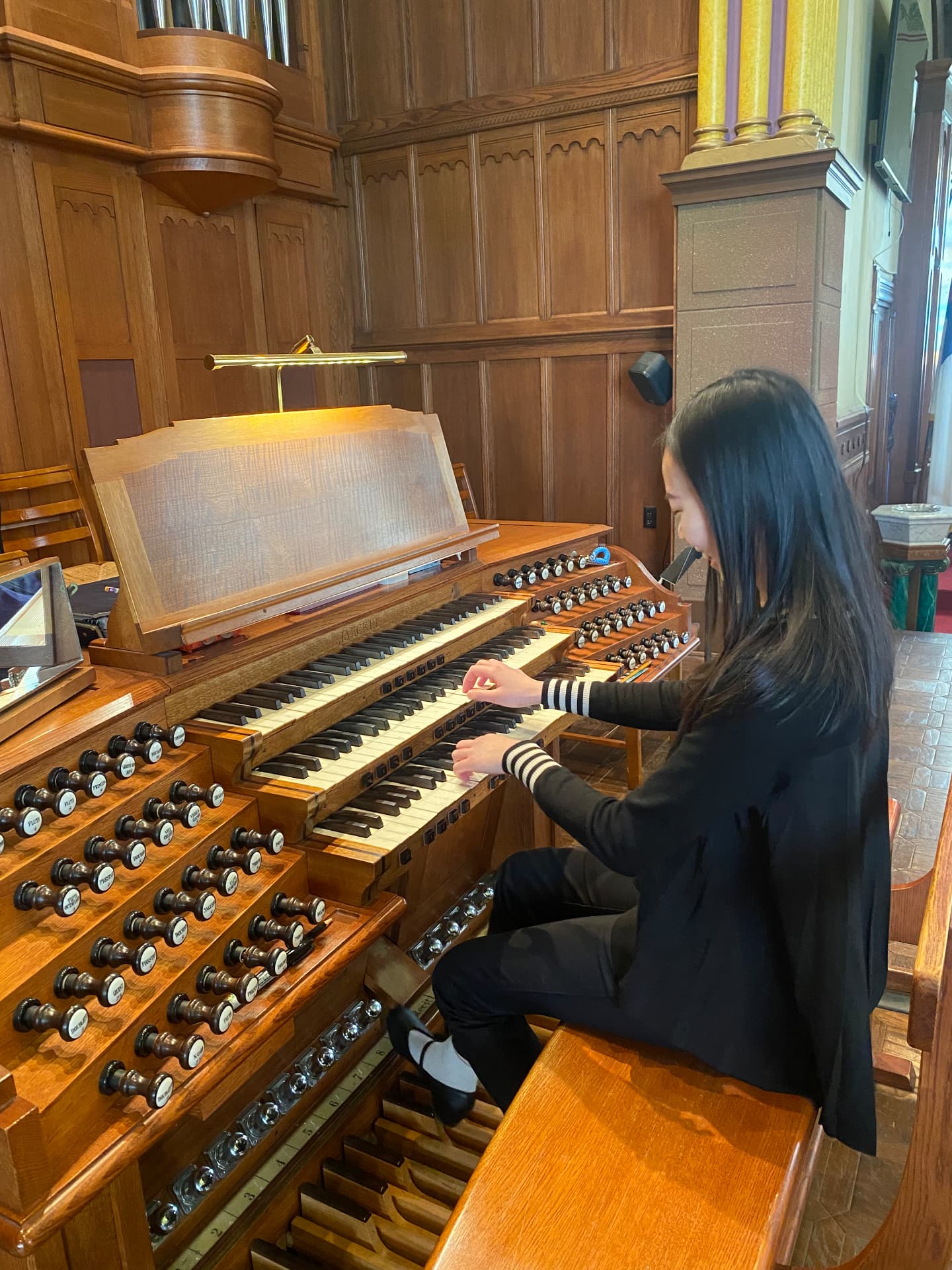 Yi-Hui Chen seated at the pipe organ console in a church, smiling