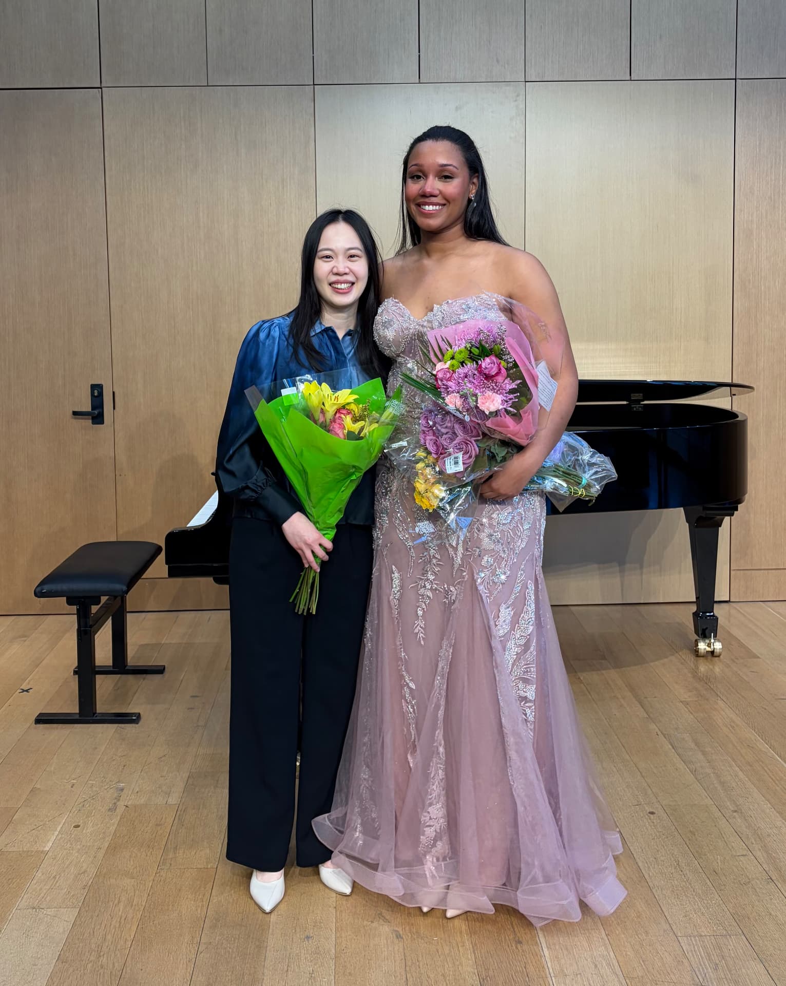 Yi-Hui Chen with a singer holding bouquets after a recital in front of a grand piano